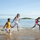 A mother and two kids run along the beach while laughing together in Fiji