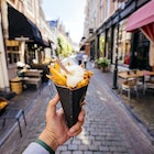 1440601751
A man holds out a cone filled with frites on an Amsterdam street