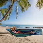 Woman with headphones lying on a hammock at the beach, Kadavu island, Fiji