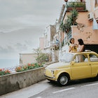 Two beautiful young woman inside a small, vintage yellow car. The top remains open. They stand up in the vehicle, through the sunroof and take photos of each other. We can see Italy's famous view of Positano in the background. Depicts a scene of experiential travel, suggesting renting a car, travel tours, European road trips and nostalgia.
1492413341