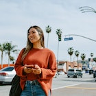 A young woman standing on a street in LA holding her phone.