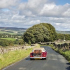 Little red car driving near Aysgarth in the Yorkshire Dales on a sunny September day. Bolton castle seen in the far distance.