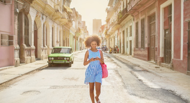 A woman walking along a street in Havana while looking at her phone