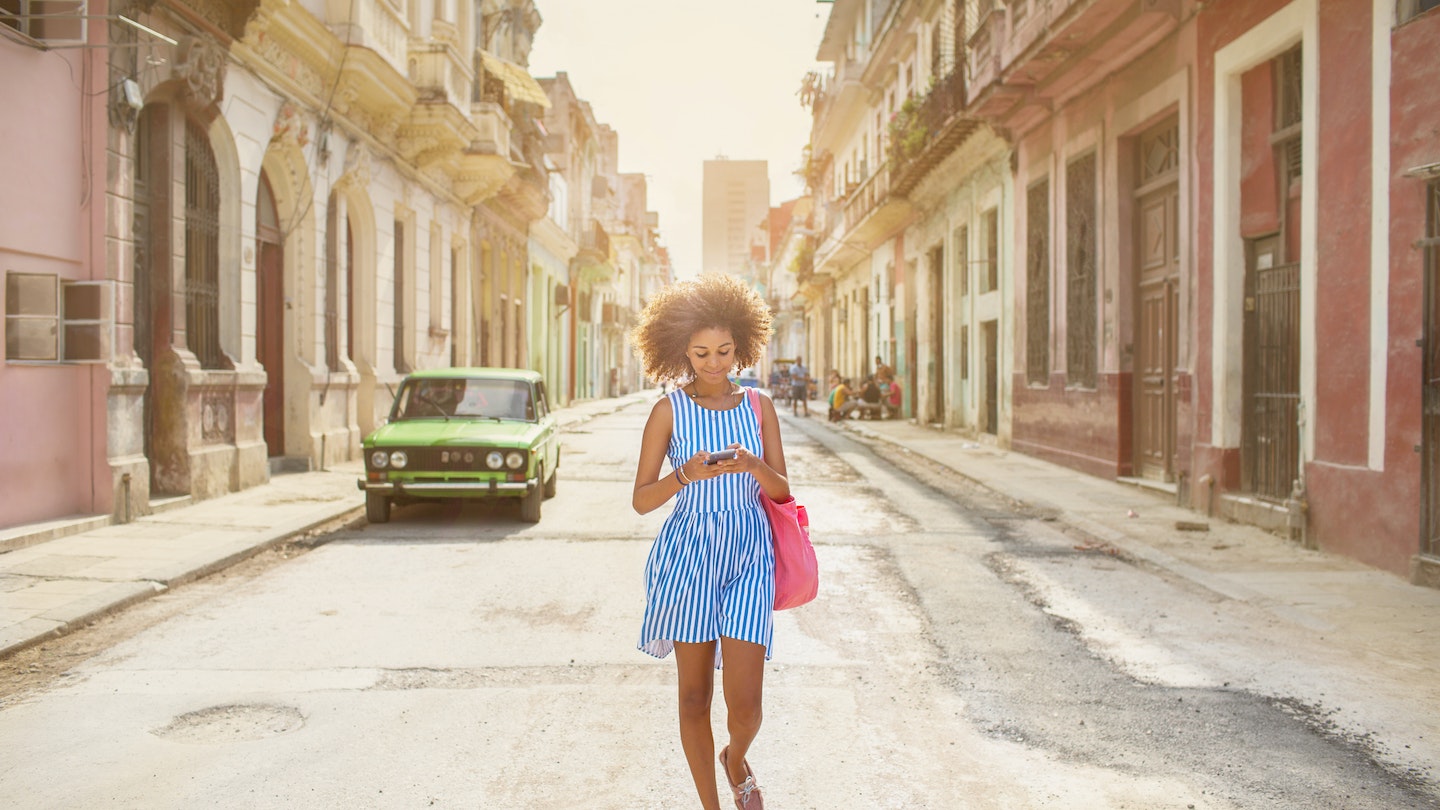 A woman walking along a street in Havana while looking at her phone