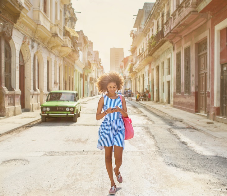 A woman walking along a street in Havana while looking at her phone