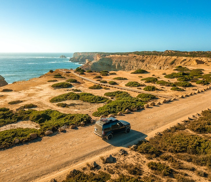 Algarve, Portugal - August 2020: Lifestyle photo of a black Land Rover Discovery 4 driving along scenic Portuguese coastline.; Shutterstock ID 1912082461; your: Brian Healy; gl: 65050; netsuite: Lonely Planet Online Editorial; full: Best road trips in Portugal