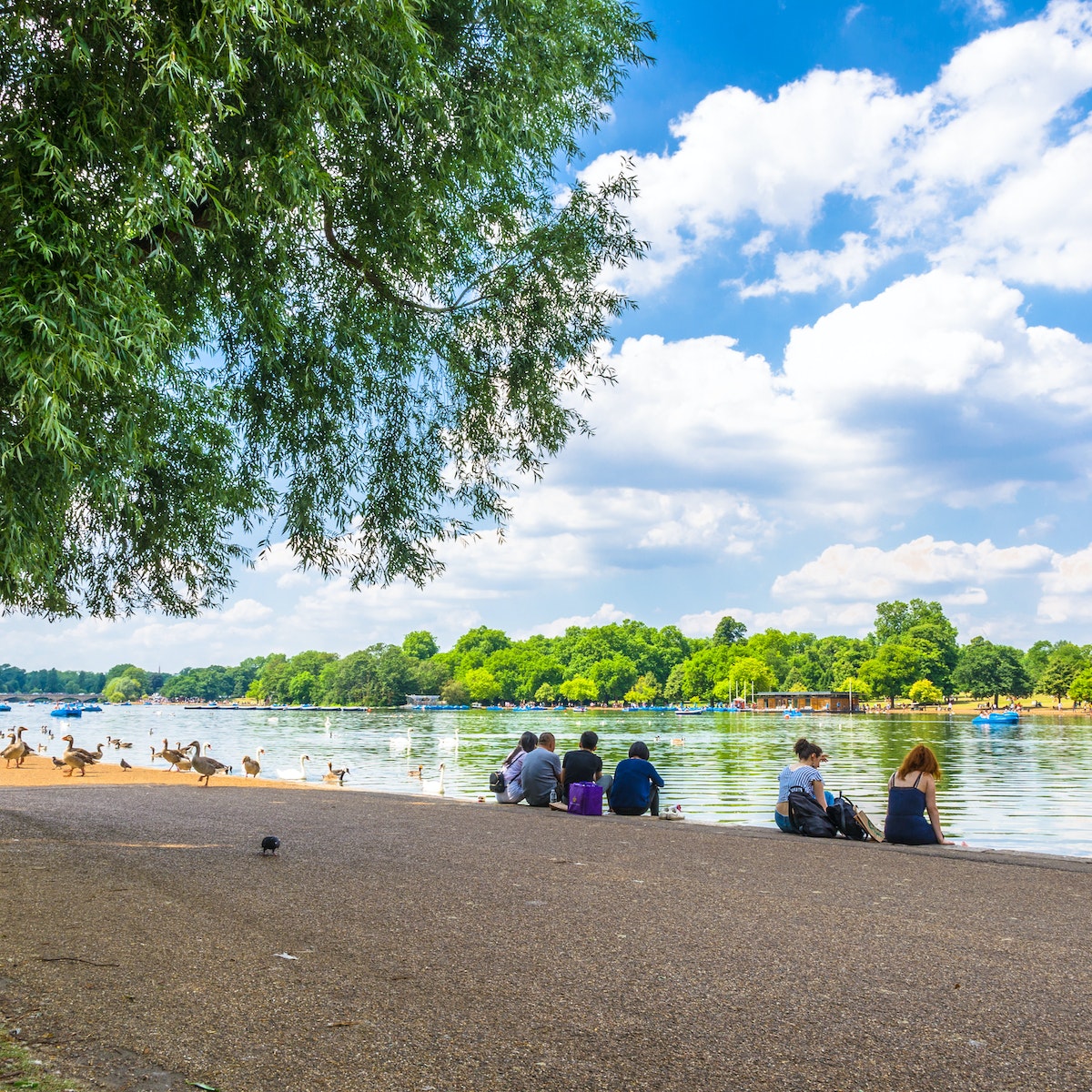 JUNE 18, 2017: Visitors seated on the shore of Serpentine Lake in Hyde Park.