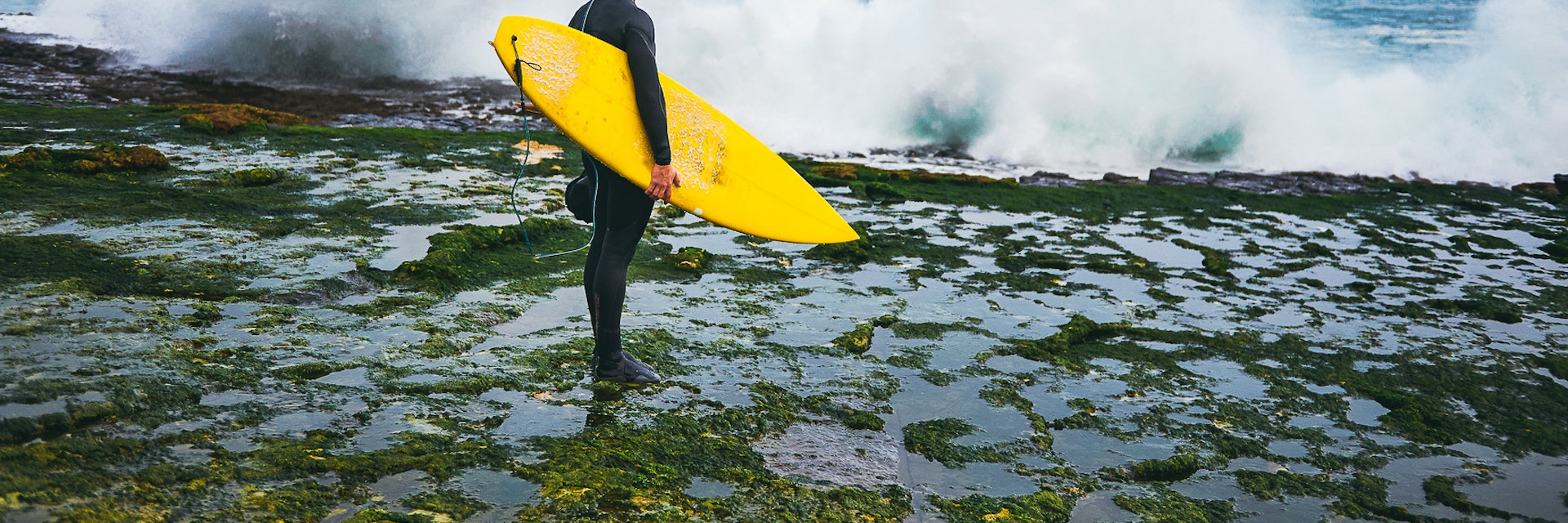 Surfer looking at the waves crushing on the cliff during winter surfing session