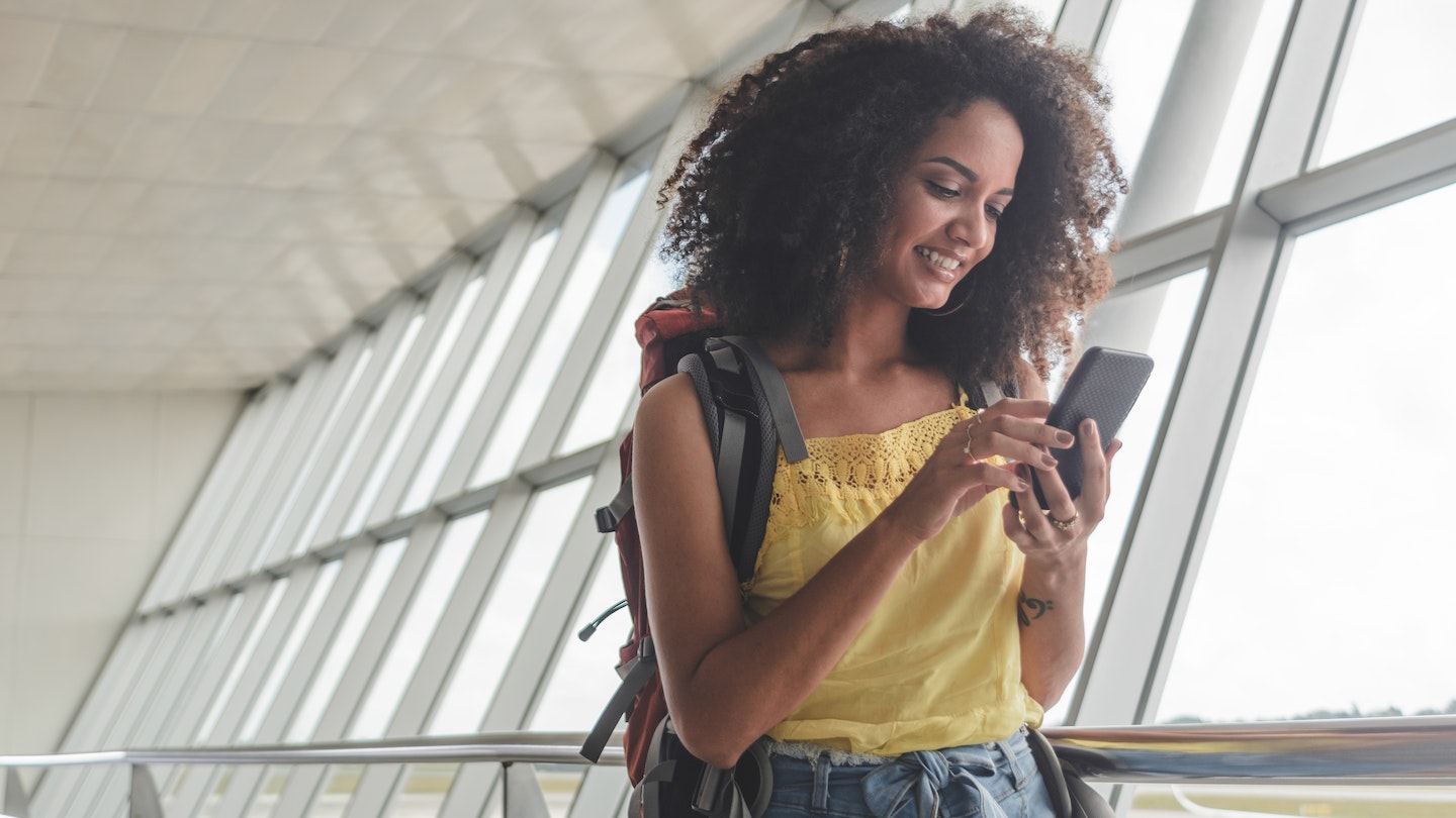 Young woman with backpack checking her boarding schedule at an airport. 